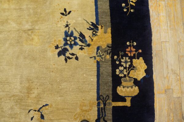 Light tan and navy blue rug with stylized florals and a vase motif sits on distressed wood planks.