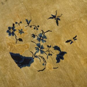 Gold pile rug with a navy and ochre floral pattern featuring small butterfly motifs.