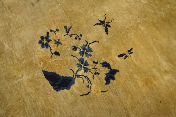 Gold pile rug with a navy and ochre floral pattern featuring small butterfly motifs.