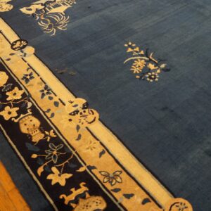 Low-pile indigo rug with gold and dark blue floral borders lies across bright wooden plank flooring.