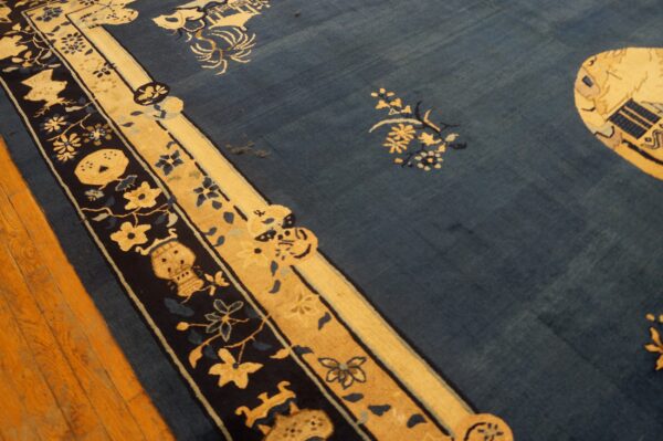 Low-pile indigo rug with gold and dark blue floral borders lies across bright wooden plank flooring.