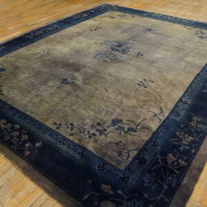 Faded gray-green rug with scattered floral designs and a wide navy border sits on light hardwood flooring.