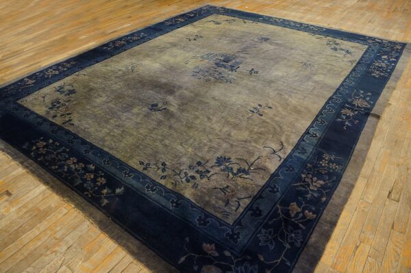 Faded gray-green rug with scattered floral designs and a wide navy border sits on light hardwood flooring.