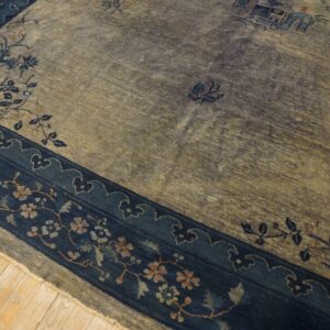 Muted gold and gray field rug with a wide navy blue floral border resting on light wood planks.