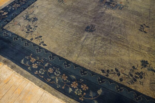 Muted gold and gray field rug with a wide navy blue floral border resting on light wood planks.