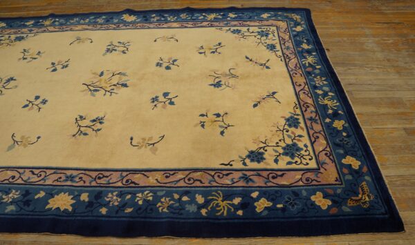 Low-pile rug in cream with scattered blue florals and a wide dark blue butterfly border on wood floors.