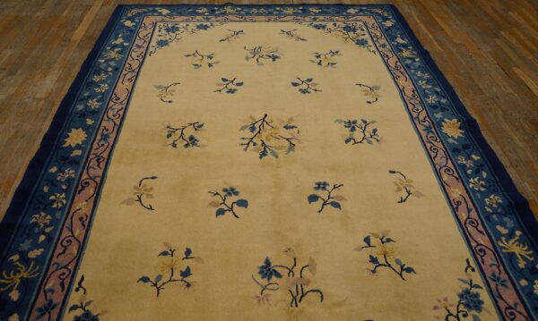 A creamy yellow rug with scattered blue and pink floral motifs, framed by multi-layered borders in navy and dusty rose.
