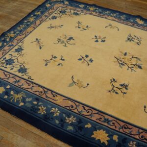Pale gold rug featuring blue and pink scattered floral motifs and wide decorative borders on hardwood.