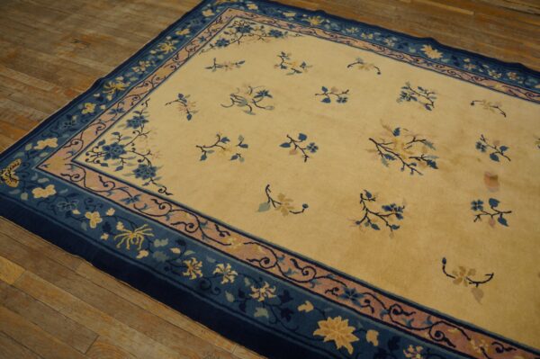Pale gold rug featuring blue and pink scattered floral motifs and wide decorative borders on hardwood.