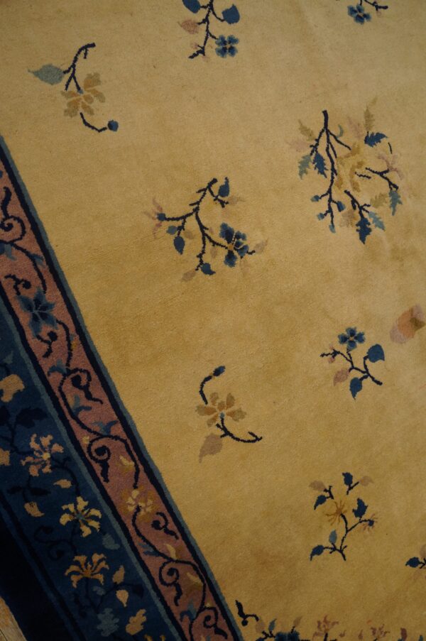 Detail of a gold rug showing sparse blue and tan florals and a contrasting blue and pink patterned border.
