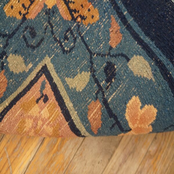 Rolled, textured rug with teal, rust, and peach floral motifs lies on light wood planks.