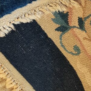A folded rug displays high blue pile, beige fringe, and a beige backing with pink and teal floral motifs.