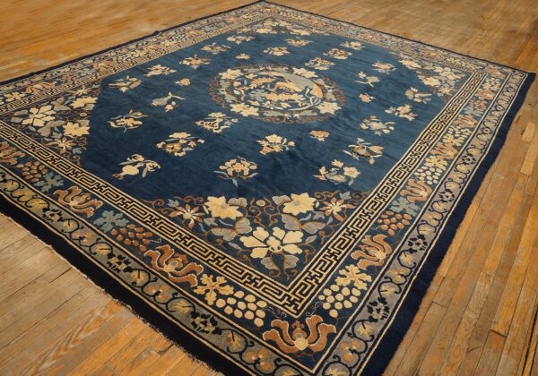 Deep indigo rug with tan, rust, and light blue floral patterns and geometric borders on wood floor.