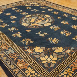 Navy blue rug with a central medallion and scattered yellow, rust, and gray floral patterns on a wood floor.
