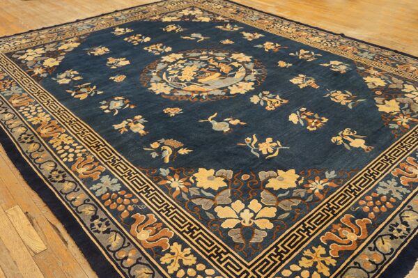 Navy blue rug with a central medallion and scattered yellow, rust, and gray floral patterns on a wood floor.