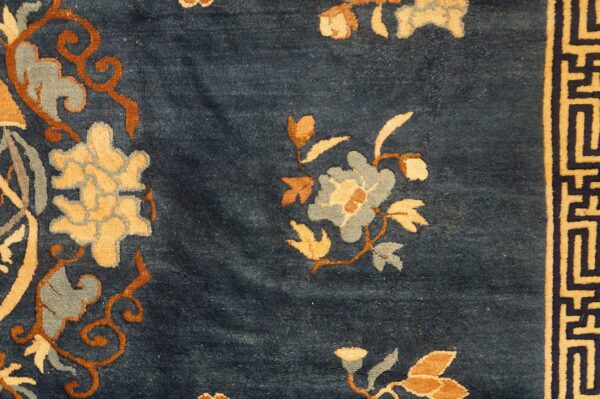 Textured blue rug featuring tan, rust, and gray floral patterns beside a thick geometric border.