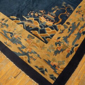 Plush navy and tan rug with an oriental landscape design lays on worn light plank wood floors.