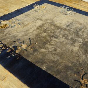 Mottled gray rug with blue and gold floral patterns features a wide navy border on distressed wooden floors.