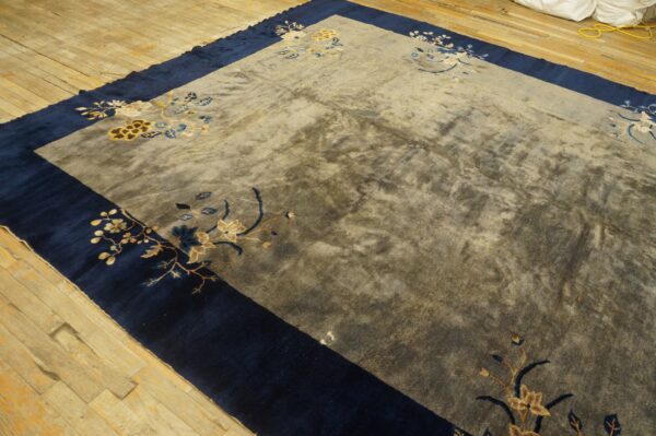 Mottled gray rug with blue and gold floral patterns features a wide navy border on distressed wooden floors.