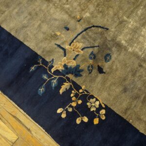 Dark blue and olive rug with gold and teal floral motifs rests on light, worn hardwood flooring.