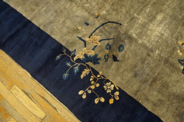 Dark blue and olive rug with gold and teal floral motifs rests on light, worn hardwood flooring.