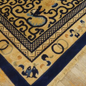 Tan and navy rug with detailed borders and animal motifs rests on distressed light wood plank flooring.