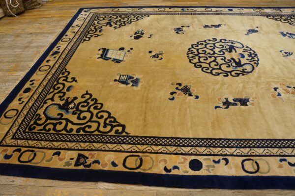 Gold area rug with dense navy blue scrollwork and multiple borders sits on wide wooden planks.
