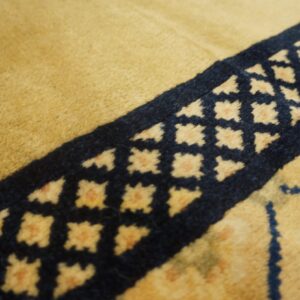 Textured detail shot showing the golden pile and a navy blue border band with light geometric diamond motifs.