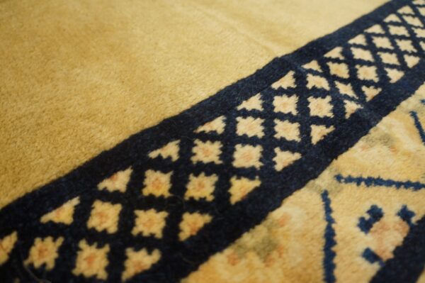 Textured detail shot showing the golden pile and a navy blue border band with light geometric diamond motifs.