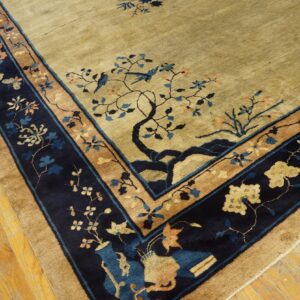 Olive beige rug with navy and tan border displaying trees, blue birds, and florals on wood floor.