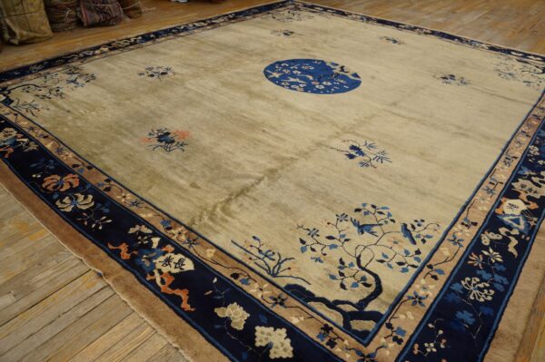 Square beige rug featuring a central blue bird medallion and scattered blue and orange floral motifs on wood floor.