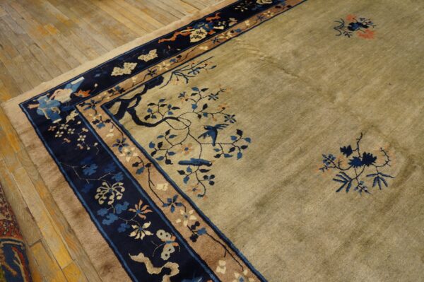 Tan and sage rug with pictorial navy blue borders showing birds and flowering branches on a rustic wood floor.