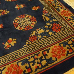 Navy rug with ornate gold and red floral and geometric borders resting on light wood flooring.