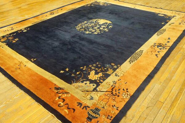 Large dark blue rug with gold and orange floral borders on reflective golden hardwood flooring.