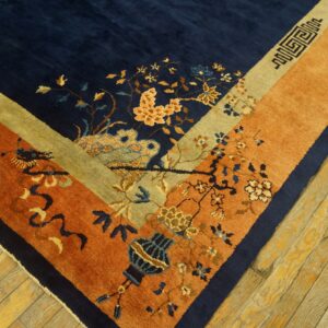 Navy blue rug corner with rust and gold borders featuring floral and geometric motifs on wood flooring.