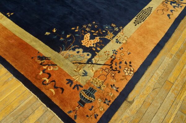 Navy blue rug corner with rust and gold borders featuring floral and geometric motifs on wood flooring.