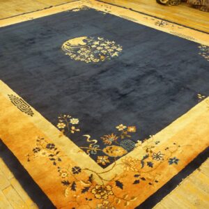 Deep blue area rug with wide saffron borders and detailed floral patterns lies on bright wooden floorboards.