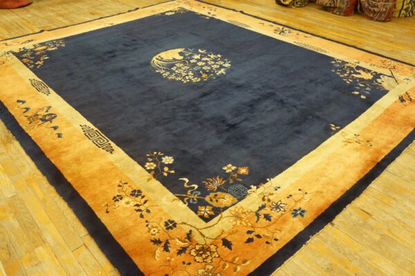 Deep blue area rug with wide saffron borders and detailed floral patterns lies on bright wooden floorboards.