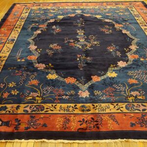 A large rug with a navy floral field, teal accents, and terracotta border sits on shiny wood floor.