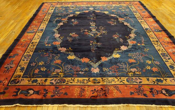 A large rug with a navy floral field, teal accents, and terracotta border sits on shiny wood floor.