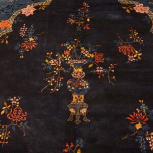 Close-up of a dark navy rug featuring a central vase of colorful flowers within a decorative yellow and blue border.