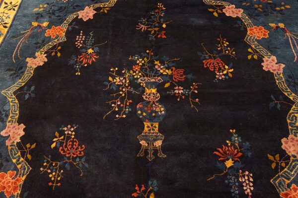 Close-up of a dark navy rug featuring a central vase of colorful flowers within a decorative yellow and blue border.