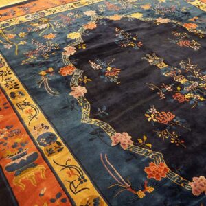 Dark navy rug with intricate floral motifs and thick rust and gold borders laid on yellow wood planking.