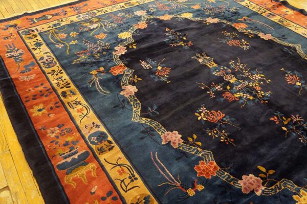 Dark navy rug with intricate floral motifs and thick rust and gold borders laid on yellow wood planking.