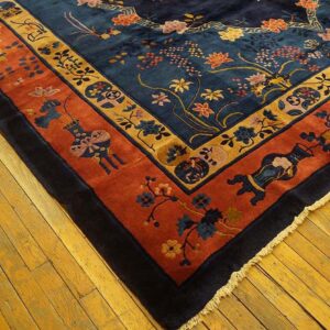 Detailed corner of a navy floral rug featuring wide terracotta and gold patterned borders on wood flooring.