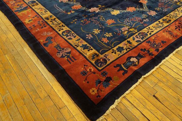 Detailed corner of a navy floral rug featuring wide terracotta and gold patterned borders on wood flooring.