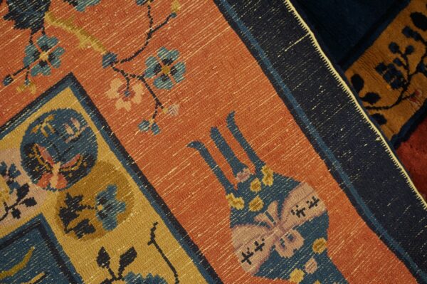 Woven detail of a rug with orange ground, featuring blue, gold, and pink geometric floral and butterfly motifs.