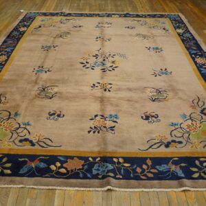 Taupe floral rug with scattered blossoms and a wide navy and gold patterned border on wood planks.