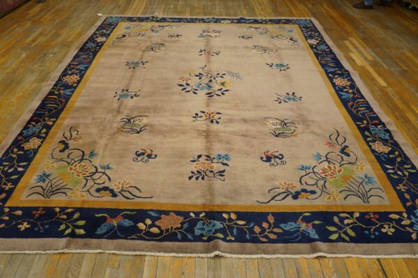 Taupe floral rug with scattered blossoms and a wide navy and gold patterned border on wood planks.