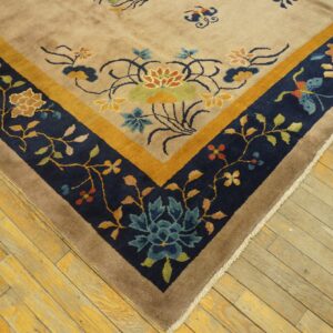 Tan rug corner with a navy, gold, and brown floral pattern border rests on rustic wood planks.